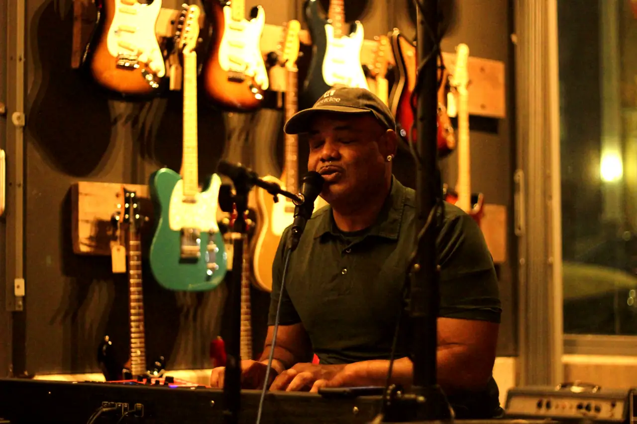 Stacey Wade singing at the keys in front of a wall of guitars