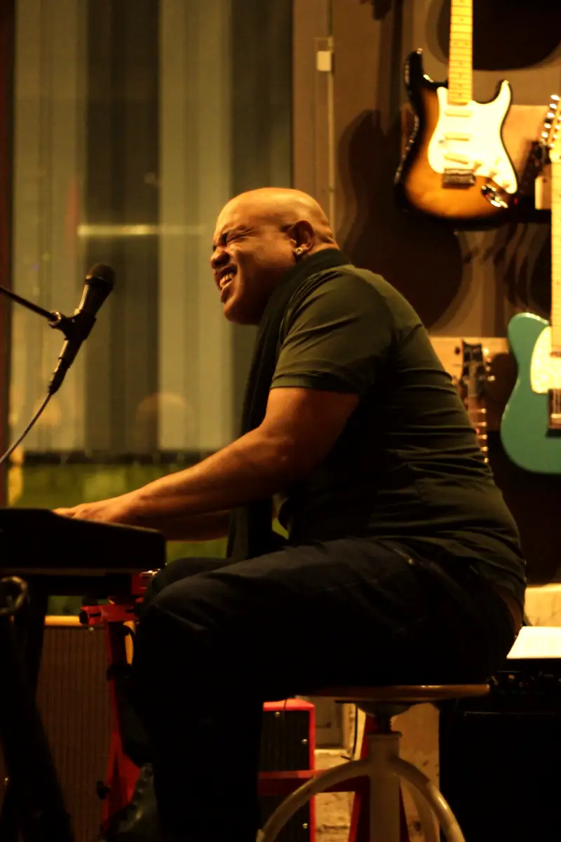 Stacey Wade laughing at the keys in front of a wall of guitars