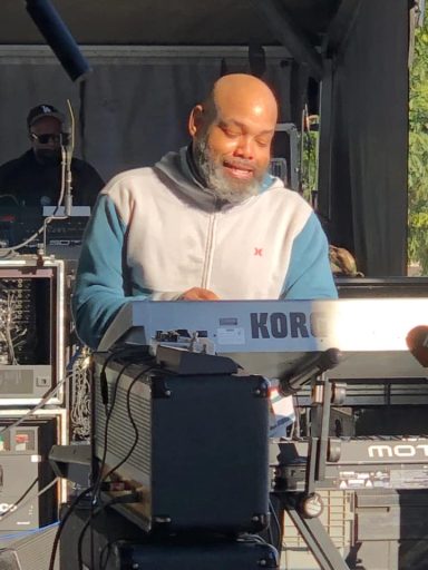 Man playing a keyboard instrument on stage with sound equipment in the background.